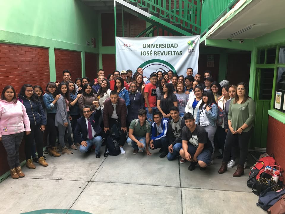 Grupo de la comunidad CUJR reunido en un patio frente a la manta institucional.